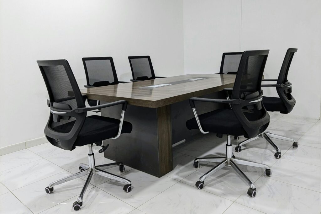 A neat and minimalistic conference room setup with black mesh chairs around a dark wooden table.